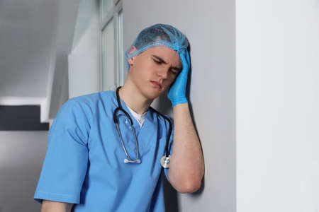 Stressed doctor near gray wall in hospital hallwayの写真素材