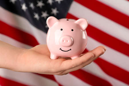 Woman holding piggy bank against American flag, closeupの写真素材