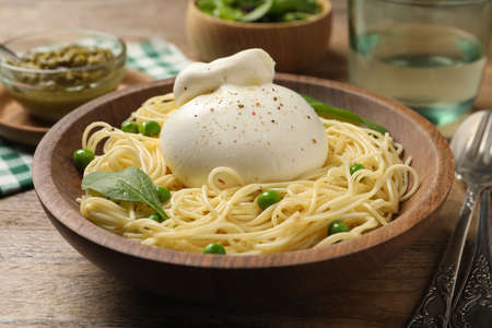 Bowl of delicious pasta with burrata, peas and spinach on wooden tableの写真素材