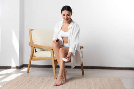 Young woman epilating her legs in roomの写真素材