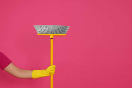 Woman holding broom on pink background, closeup. Space for text