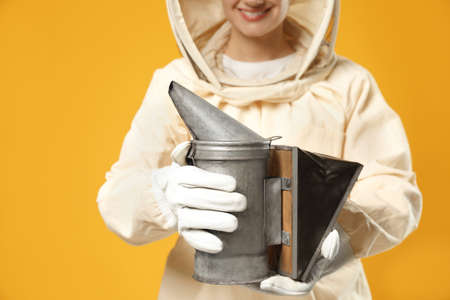 Beekeeper in uniform holding smoke pot on yellow background, closeup