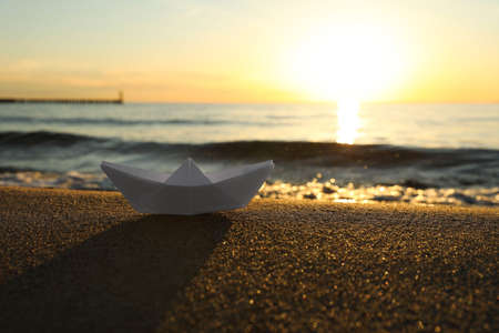 White paper boat on sand near sea at sunset, space for textの写真素材
