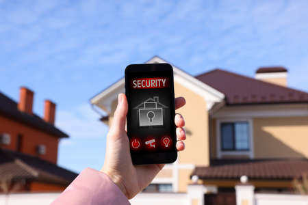 Woman using home security app on smartphone outdoors, closeupの写真素材