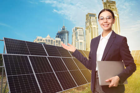 Young businesswoman with laptop near solar panels and beautiful view of cityscape. alternative energy sourcesの写真素材
