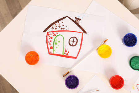 Cute children's drawing, brushes and set of paints on white table, flat lay
