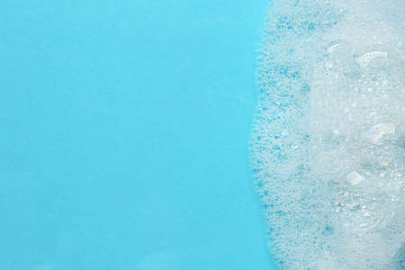 Fluffy bath foam on turquoise background, top view. Space for text
