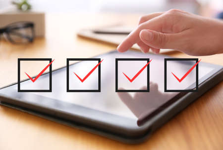 Illustration of check boxes with marks and woman using tablet at wooden table, closeup