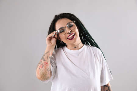 Beautiful young woman with tattoos on arms, nose piercing and dreadlocks against gray backgroundの写真素材