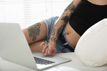 Beautiful woman with tattoos on body using laptop in living room, closeupの写真素材