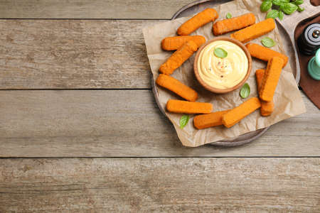 Delicious chicken nuggets and cheese sauce with basil on wooden table, flat lay. Space for textの写真素材