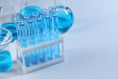 Laboratory glassware with blue liquid on light background. Space for text