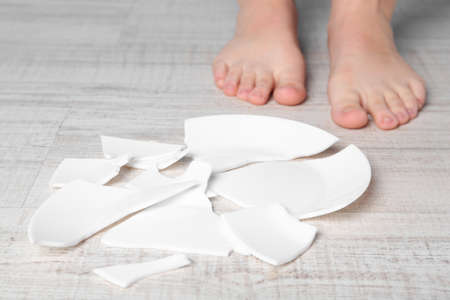 Barefoot woman standing near broken plate on floor, closeup