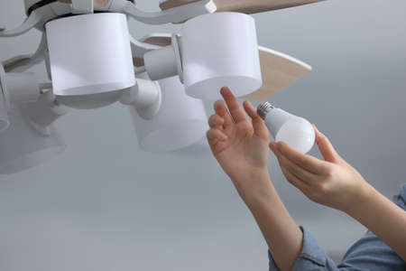 Woman changing fluorescent light bulb in ceiling lamp at home, closeup. Saving energy concept