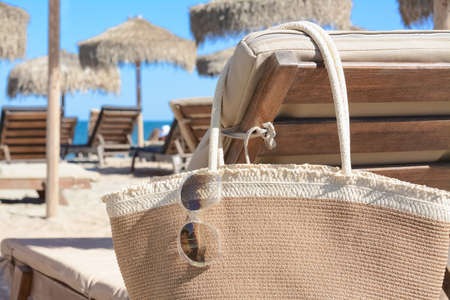 Straw bag with sunglasses on wooden sunbed near sea, closeup. beach accessoriesの写真素材