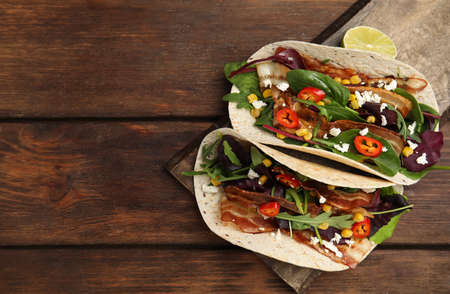 Delicious tacos with fried bacon, vegetables and cheese on wooden table, top view. Space for textの写真素材
