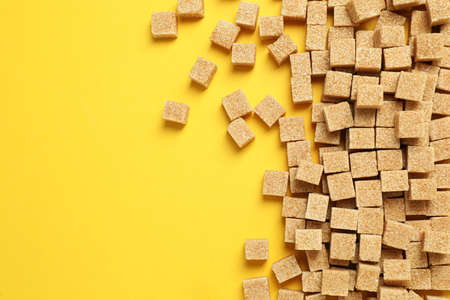Brown sugar cubes on yellow background, flat lay. Space for textの写真素材
