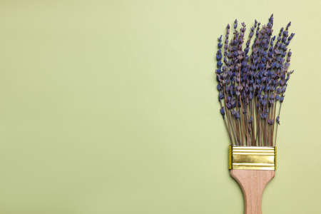 Creative flat lay composition with paint brush and lavender flowers on light green background. Space...