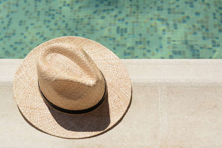 Stylish hat near outdoor swimming pool on sunny day, space for text. Beach accessoriesの写真素材