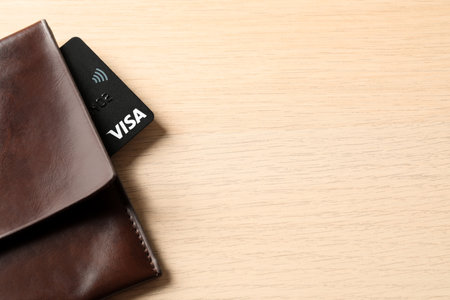 MYKOLAIV, UKRAINE - FEBRUARY 23, 2022: Bank card of Visa payment system in leather wallet on wooden table, top view. Space for textのeditorial素材