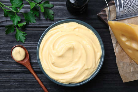 Tasty cheese sauce and parsley on black wooden table, flat layの写真素材