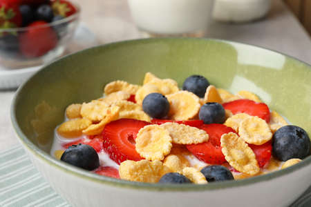 Corn flakes with berries in bowl served on gray table, closeup