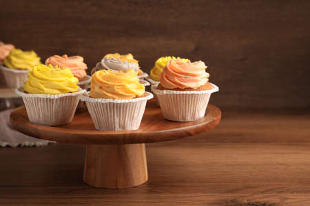 Stand with tasty cupcakes on wooden table. Space for textの写真素材