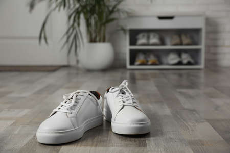 Pair of stylish white sneakers on floor in hallway, space for textの写真素材
