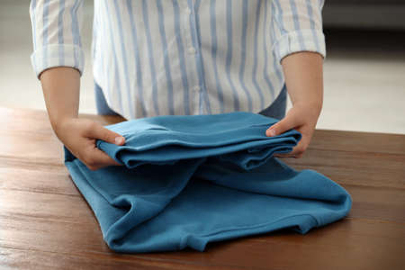 Woman folding clothes at wooden table indoors, closeupの写真素材