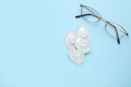 Packages with contact lenses and glasses on light blue background, flat lay. Space for textの写真素材