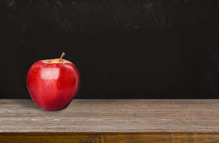 Fresh ripe red apple on wooden table near black chalkboard, space for text