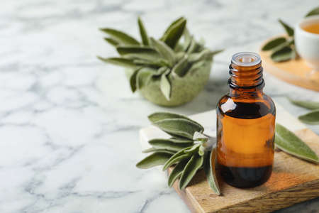 Bottle of essential sage oil and leaves on white marble table. Space for textの写真素材