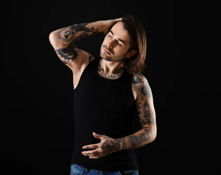 Young man with tattoos on body against black background