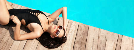 Beautiful young woman lying near swimming pool on sunny day, banner designの写真素材