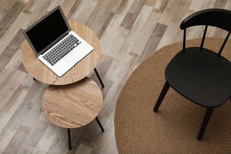 Modern laptop on wooden nesting table near black chair indoors, above view