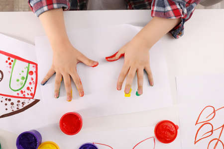 Little child making hand prints on paper with painted palms at white table, top viewの写真素材