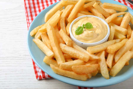 Delicious French fries and cheese sauce with basil on white wooden table, closeup