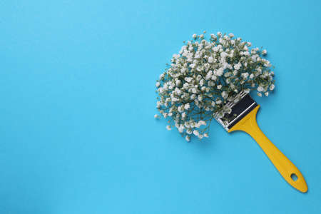 Creative composition with paint brush and gypsophila flowers on light blue background, top view....