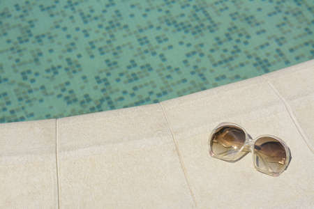Stylish sunglasses near outdoor swimming pool on sunny day, space for text. Beach accessoriesの写真素材