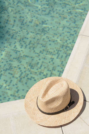 Stylish hat near outdoor swimming pool on sunny day, space for text. Beach accessoriesの写真素材