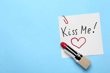Card with phrase Kiss Me and drawn heart, lipstick on light blue background, top view. Space for textの写真素材