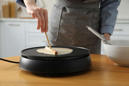 Woman cooking delicious crepe on electrical pancake maker in kitchen, closeupの写真素材