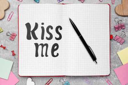 Phrase Kiss me written in notebook and stationery on light gray stone table, flat layの写真素材