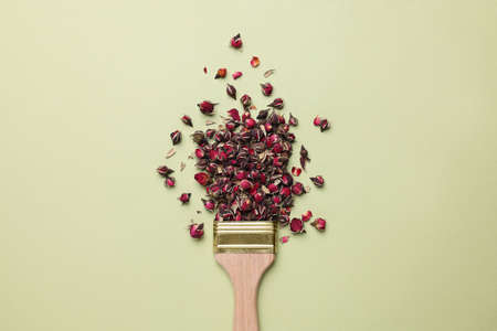 Creative flat lay composition with paint brush and dried rose buds on light green backgroundの写真素材