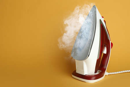 Modern iron with steam on orange background, space for textの写真素材