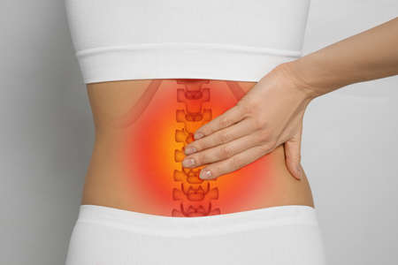 Woman suffering from pain in back on light gray background, closeup