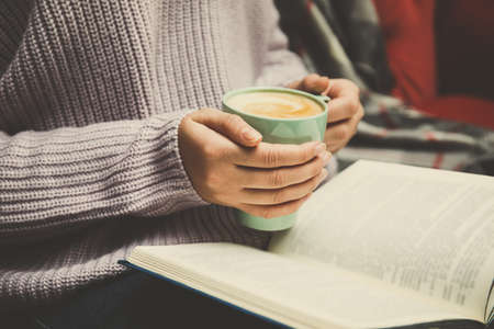 Woman with cup of coffee reading book at home, closeupの写真素材