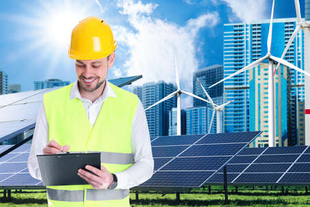 Industrial engineer in uniform and view of solar panels and wind energy turbines installed outdoors