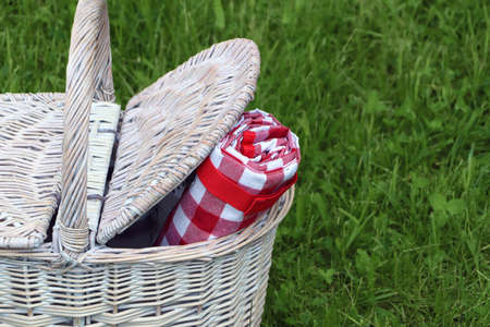 Rolled checkered tablecloth in picnic basket on green grass outdoors, closeup. Space for textの写真素材
