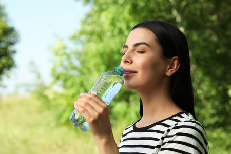Young woman drinking water outdoors. Refreshing drinks